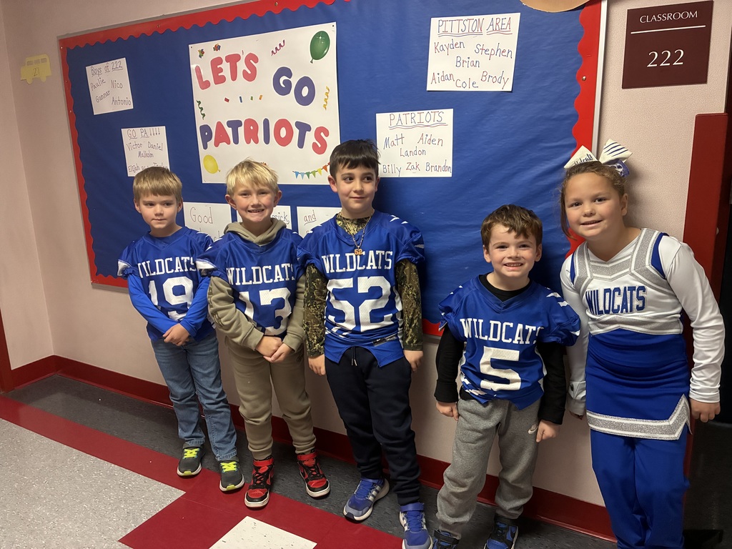 Wildcat football players and cheerleaders smiling at the camera in the school hallway.