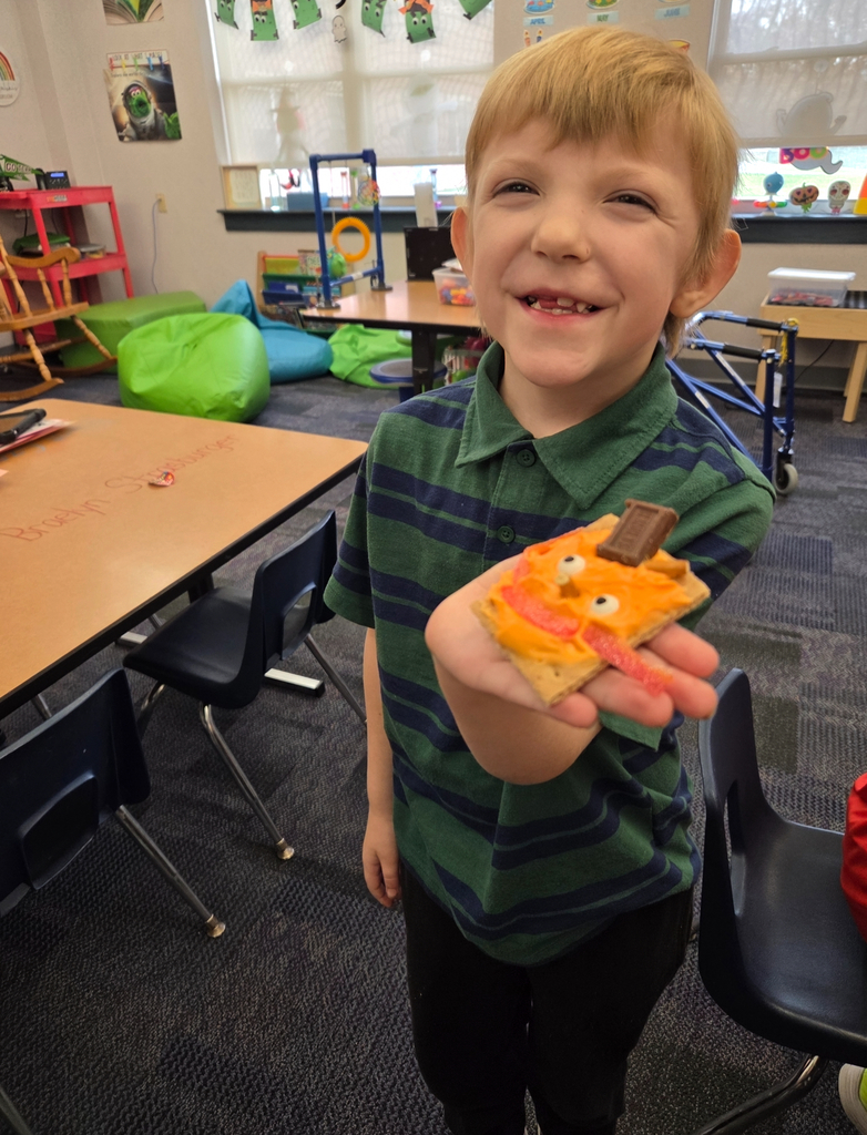 A student holding a square graham cracker decorated like an orange pumpkin.