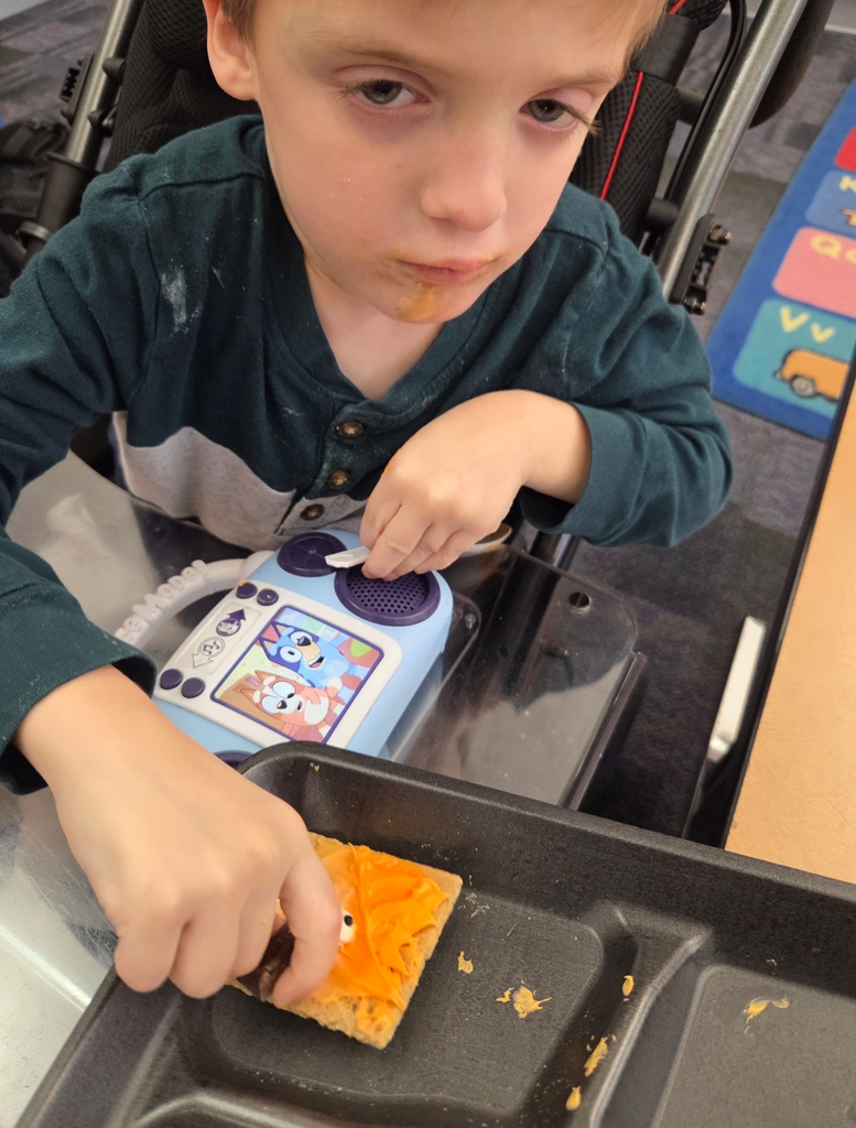 A student holding a square graham cracker decorated like an orange pumpkin.