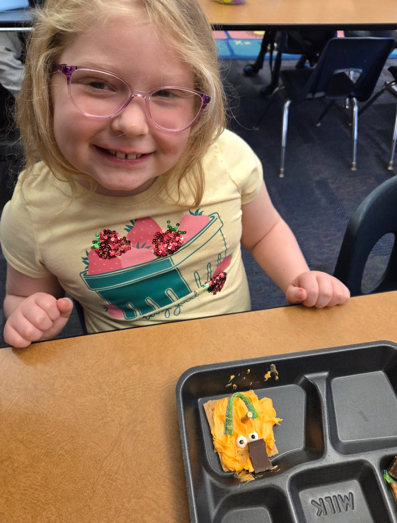 A student holding a square graham cracker decorated like an orange pumpkin.