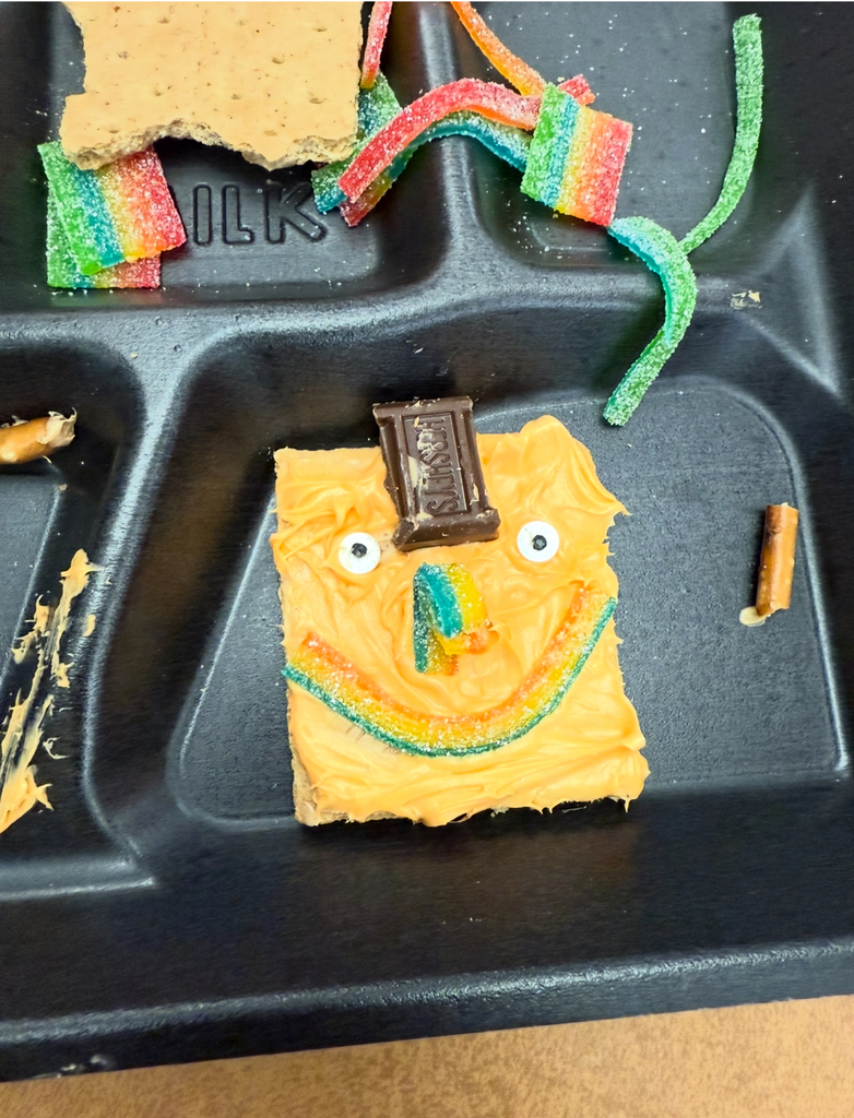A student holding a square graham cracker decorated like an orange pumpkin.