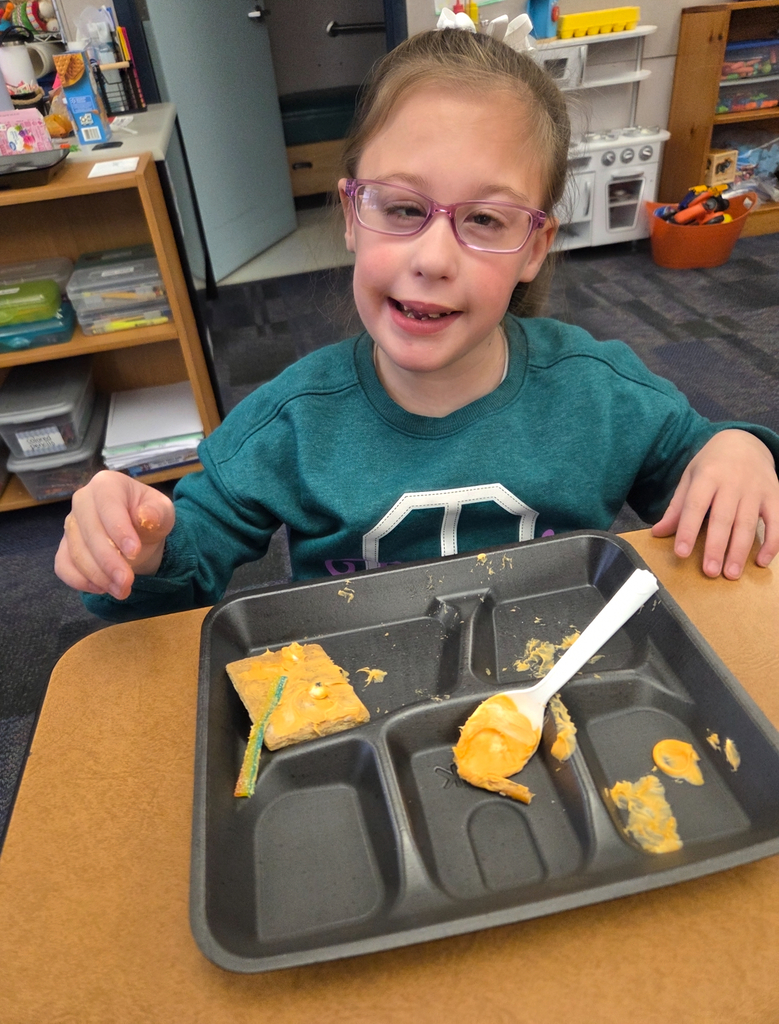 A student holding a square graham cracker decorated like an orange pumpkin.