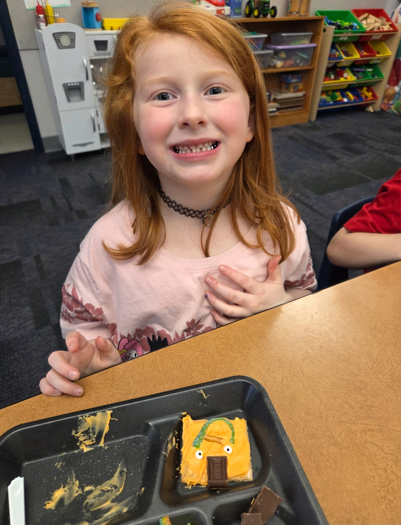 A student holding a square graham cracker decorated like an orange pumpkin.