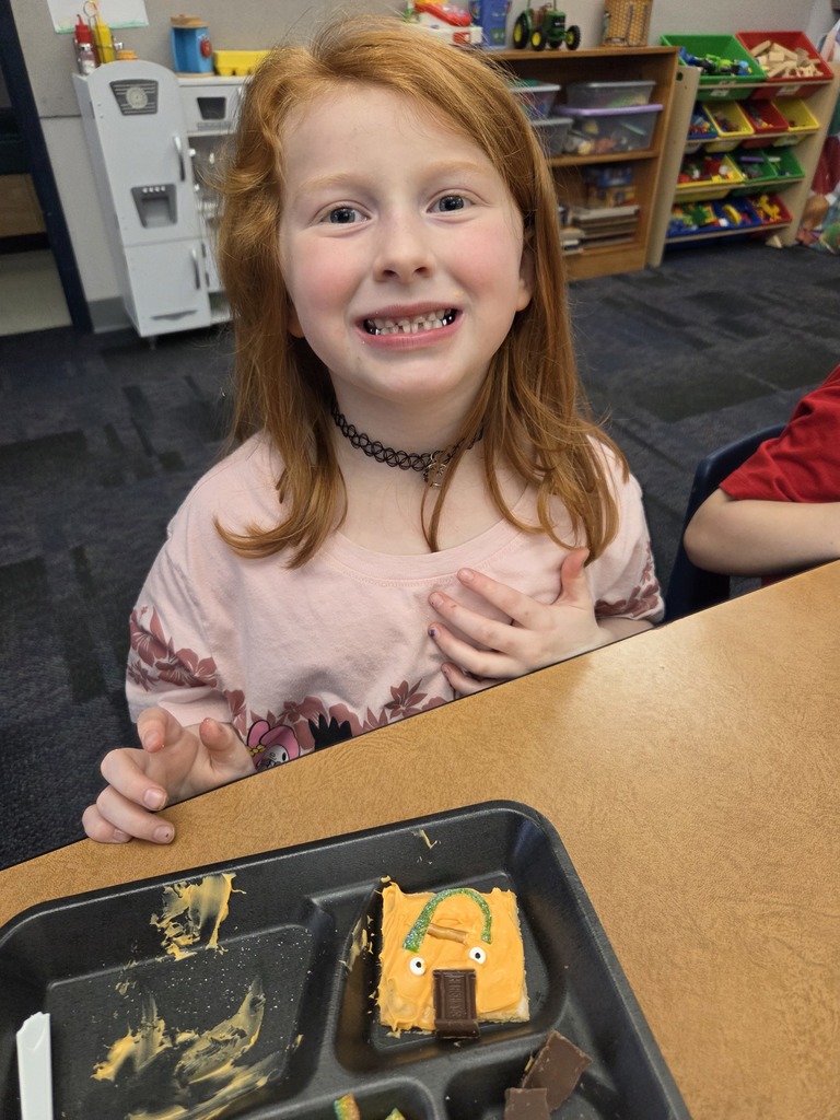 A student holding a square graham cracker decorated like an orange pumpkin.