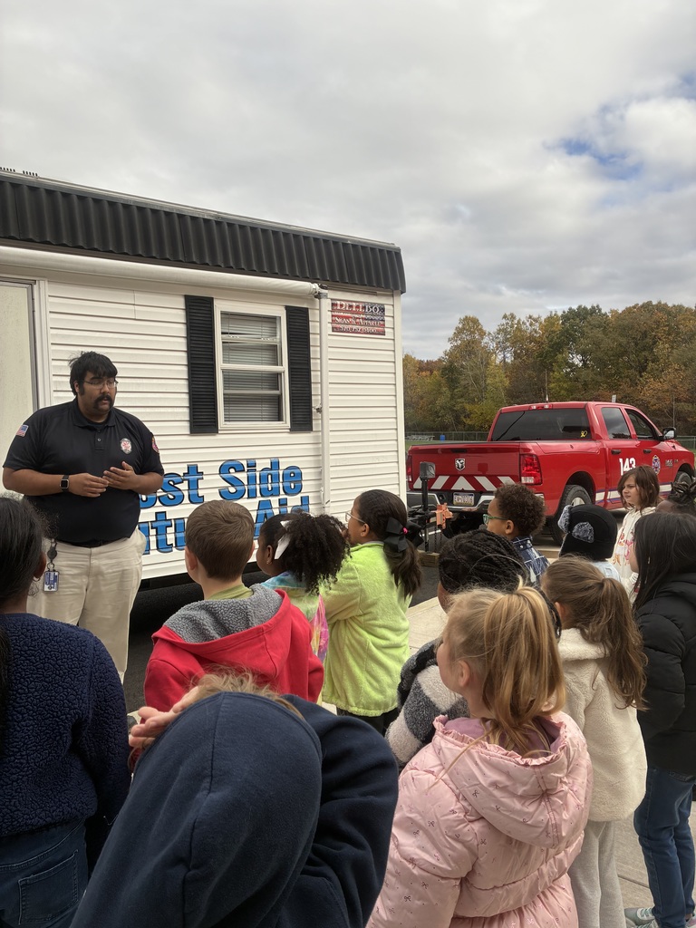 A fireman talking to a group of students in-front of a smokehouse.