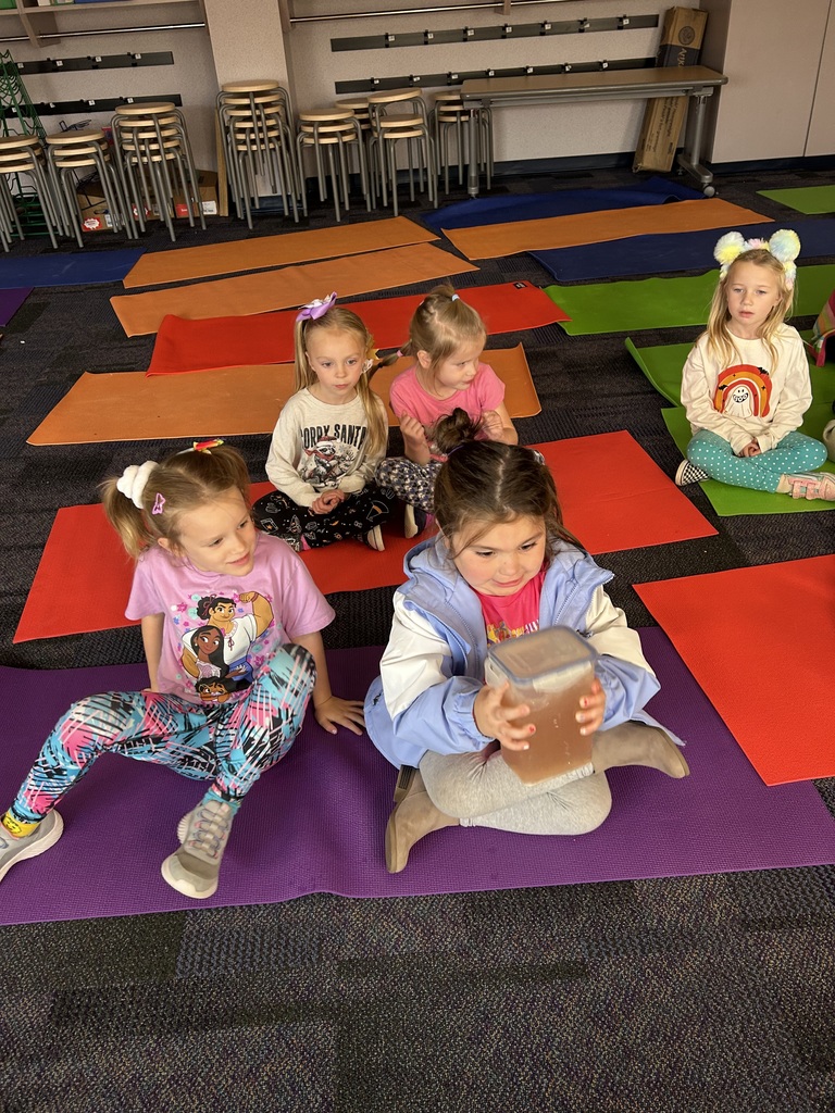 Kids sitting on yoga mats. A girl holding a jar of nutrients.