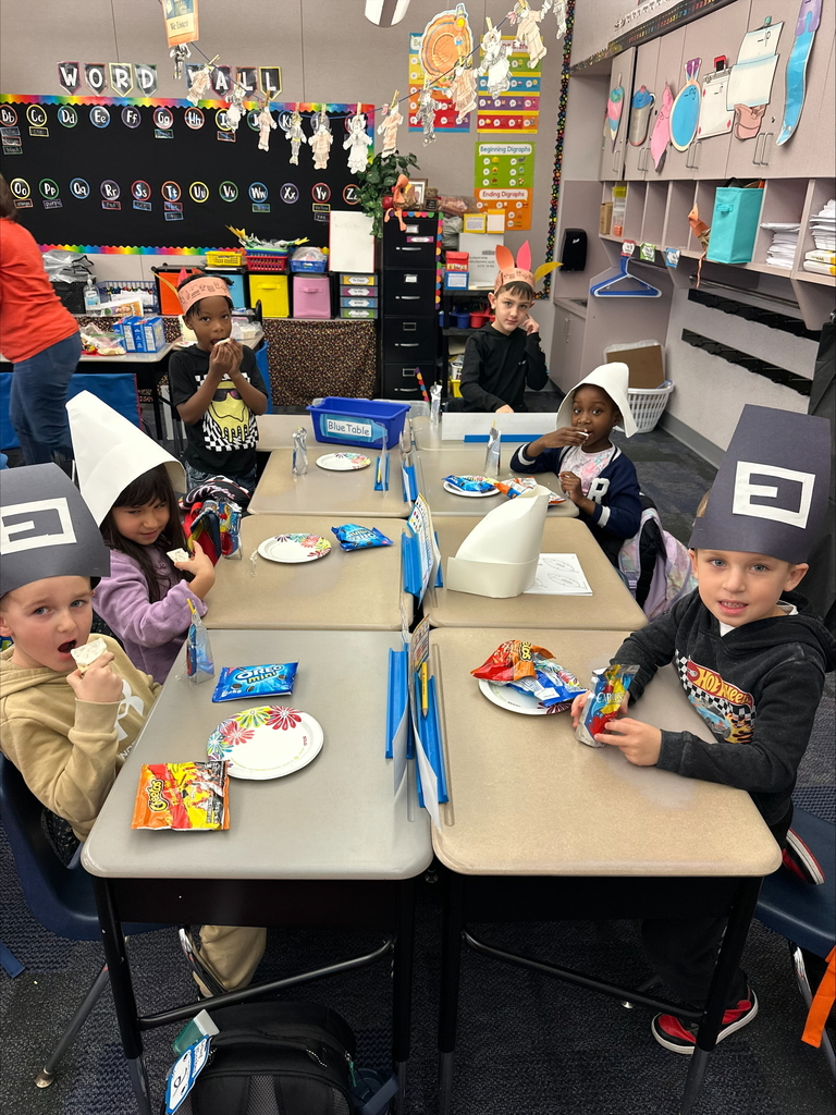 Kindergarten students seated wearing pilgrim hats and feathered head dresses