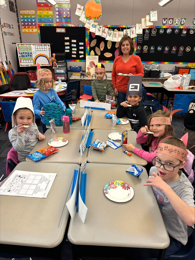 Kindergarten students seated wearing pilgrim hats and feathered head dresses