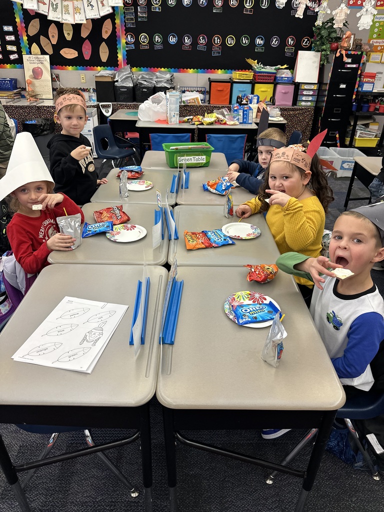 Kindergarten students seated wearing pilgrim hats and feathered head dresses