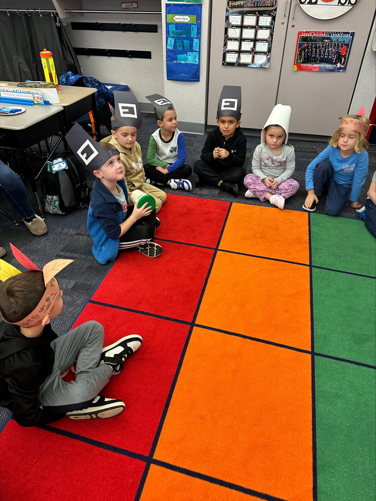 Kindergarten students seated wearing pilgrim hats and feathered head dresses