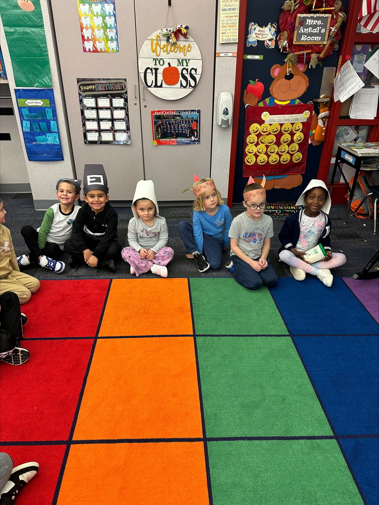 Kindergarten students seated wearing pilgrim hats and feathered head dresses