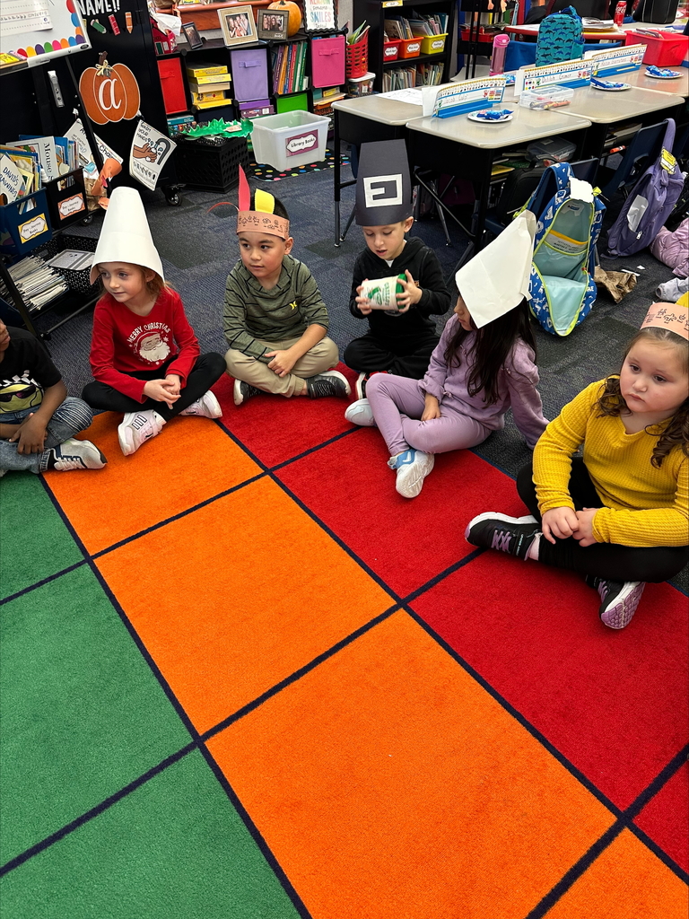 Kindergarten students seated wearing pilgrim hats and feathered head dresses