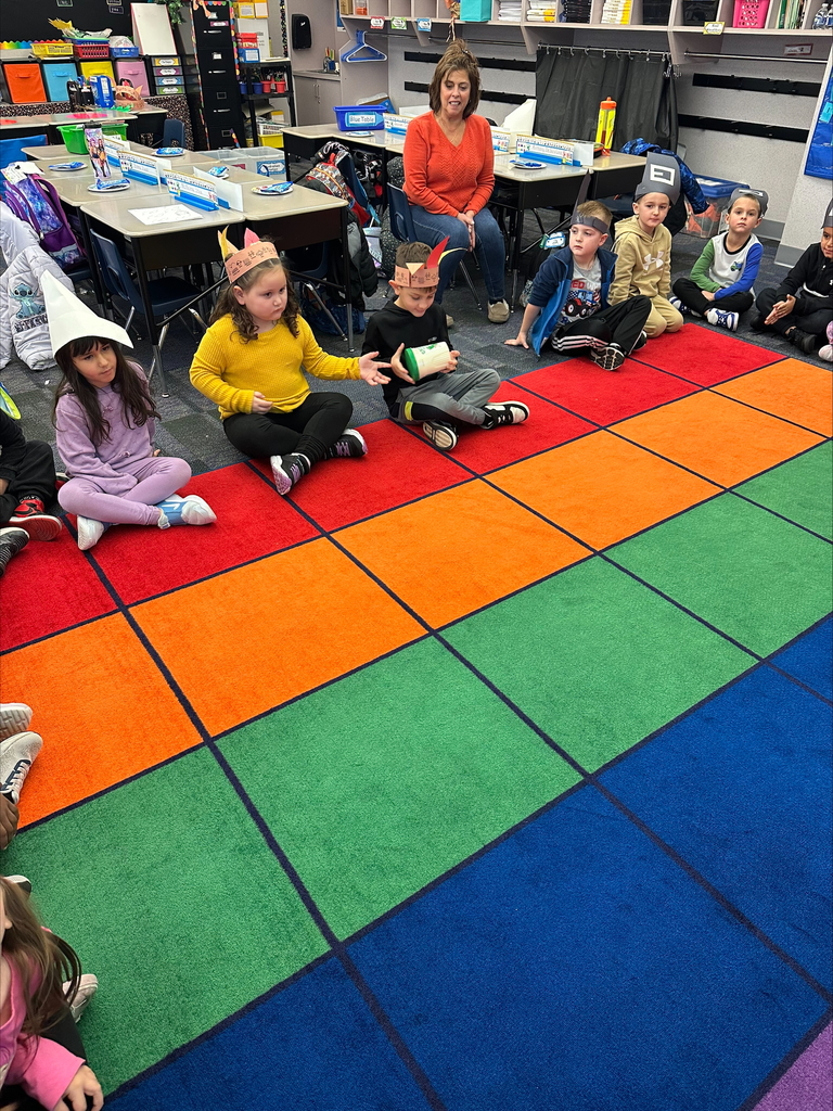 Kindergarten students seated wearing pilgrim hats and feathered head dresses