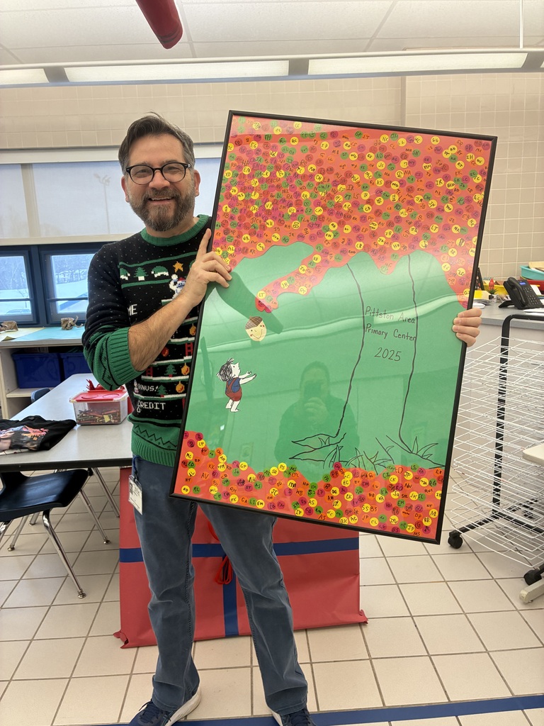Mr. Weber in the art room holding a student made giving tree poster