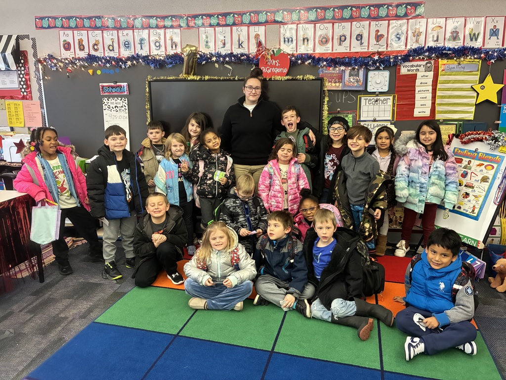 Miss Pedana smiling in a classroom with first grade students