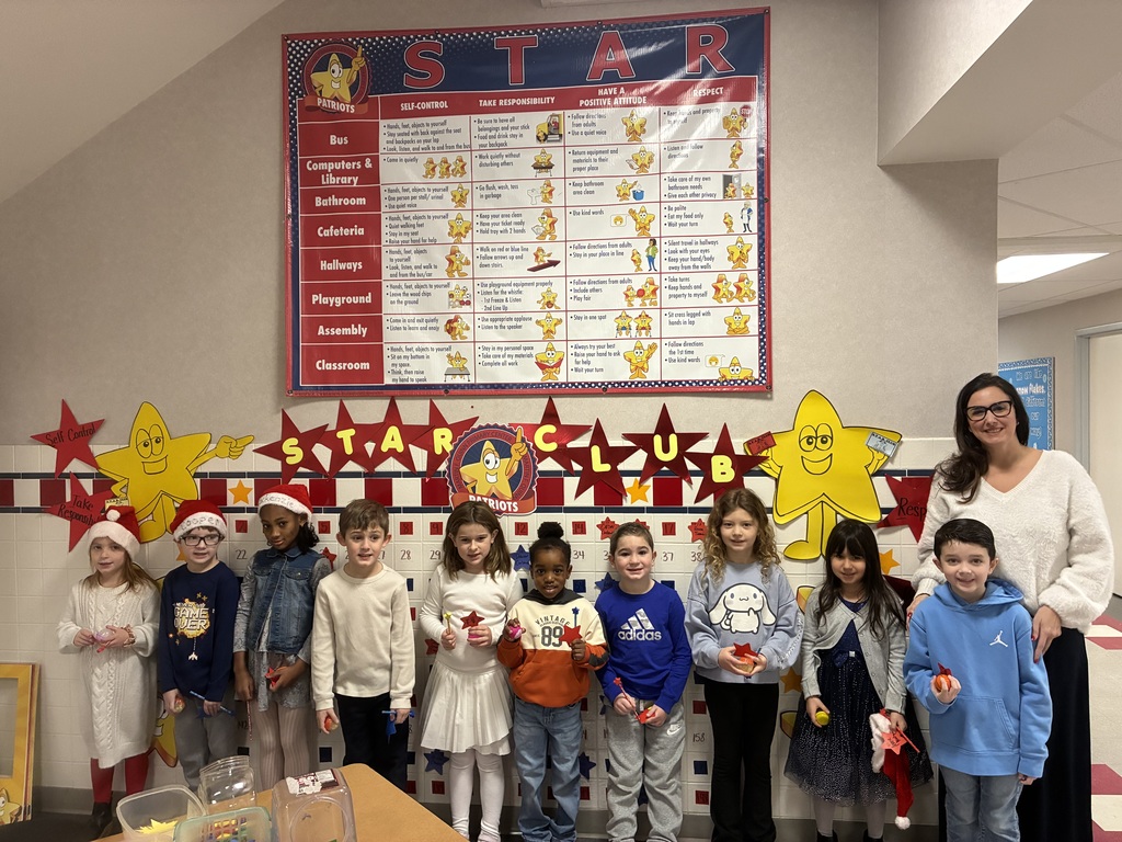A group of students standing in front of a star club bingo board sniling holding prizes. 