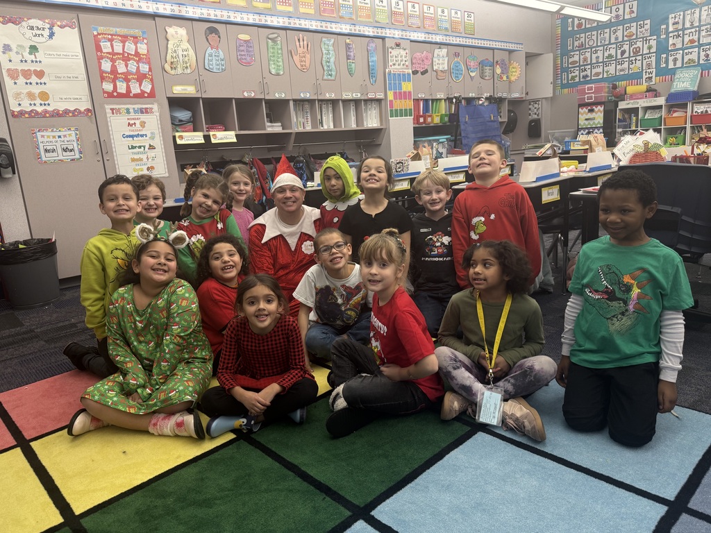 A group of students dressed in grinch clothes seated around a man dressed as an elf. 