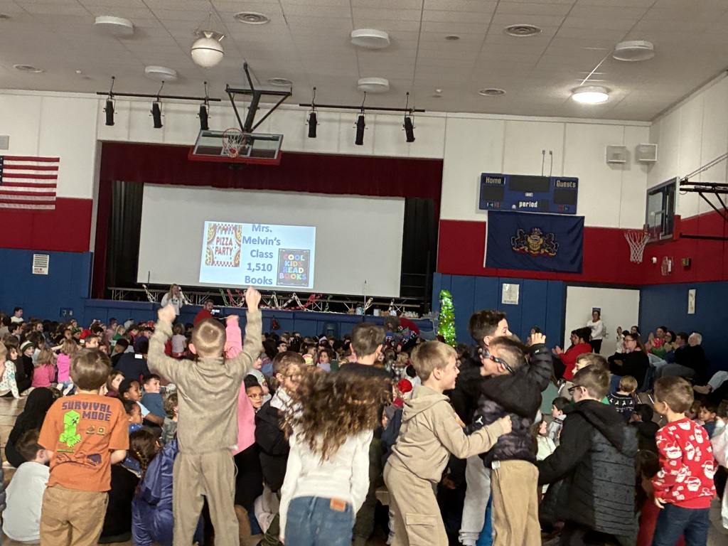 Students in a assembly in the gym with a slide projected with top readers.  