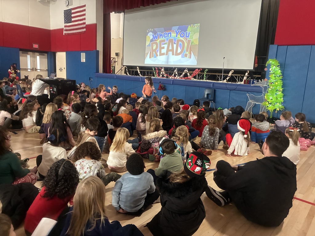 Students in a assembly in the gym with a slide projected with top readers.  