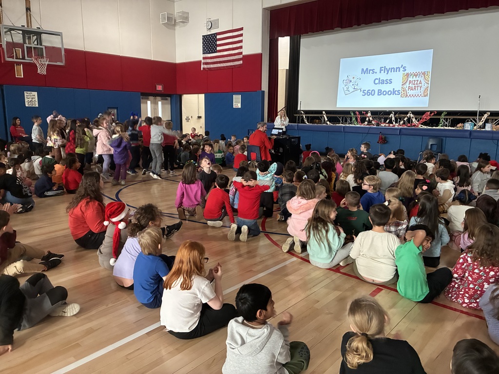 Students in a assembly in the gym with a slide projected with top readers.  