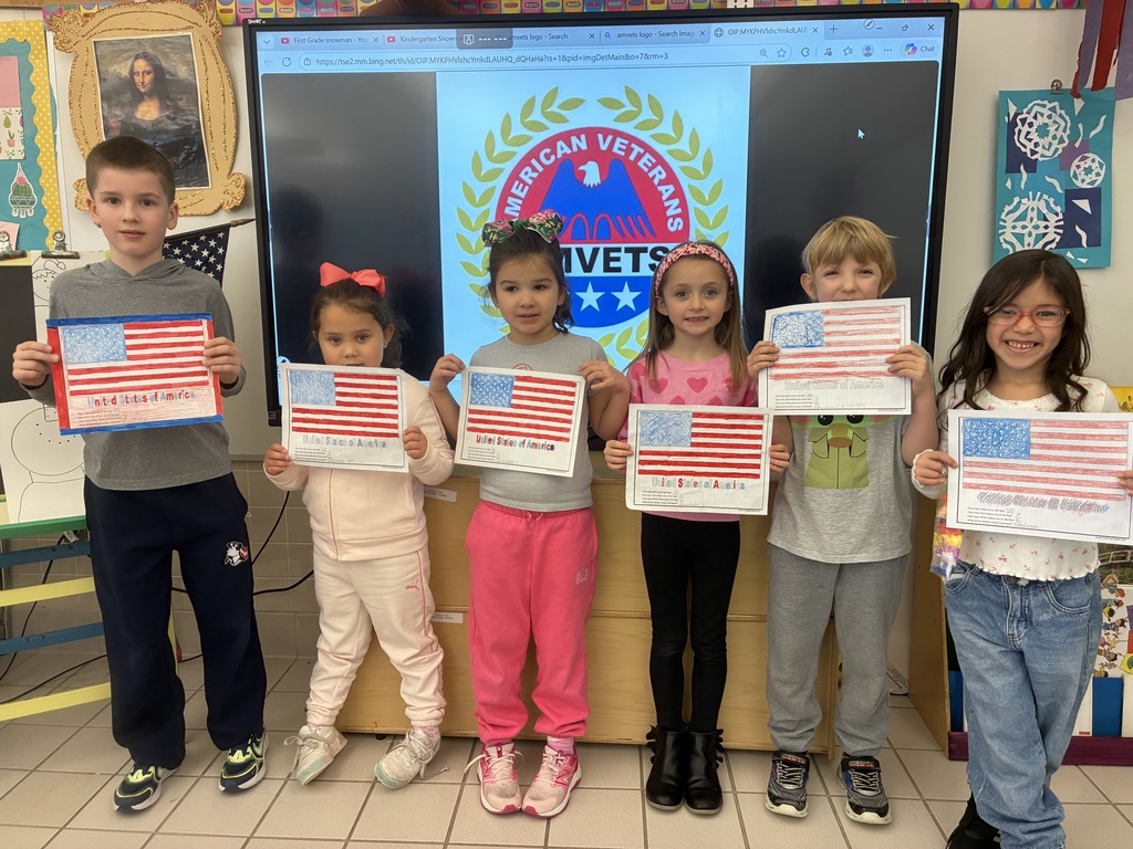 Students holding colored american flags in front of a smart board with the AMVETs logo. 
