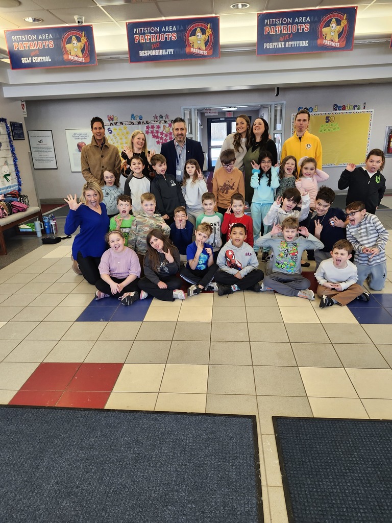 A group of second grade students with their teachers and representatives from wilkesbarre penguins posing for a picture in a group in the school lobby,