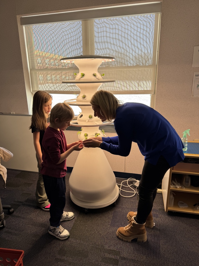Students and a teacher planting seedlings in a white hydroponic farm stand.