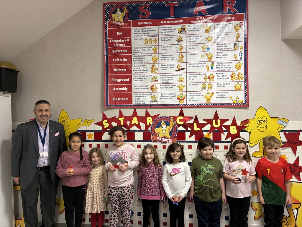 Students posing for a picture with the Principal in front of the star board