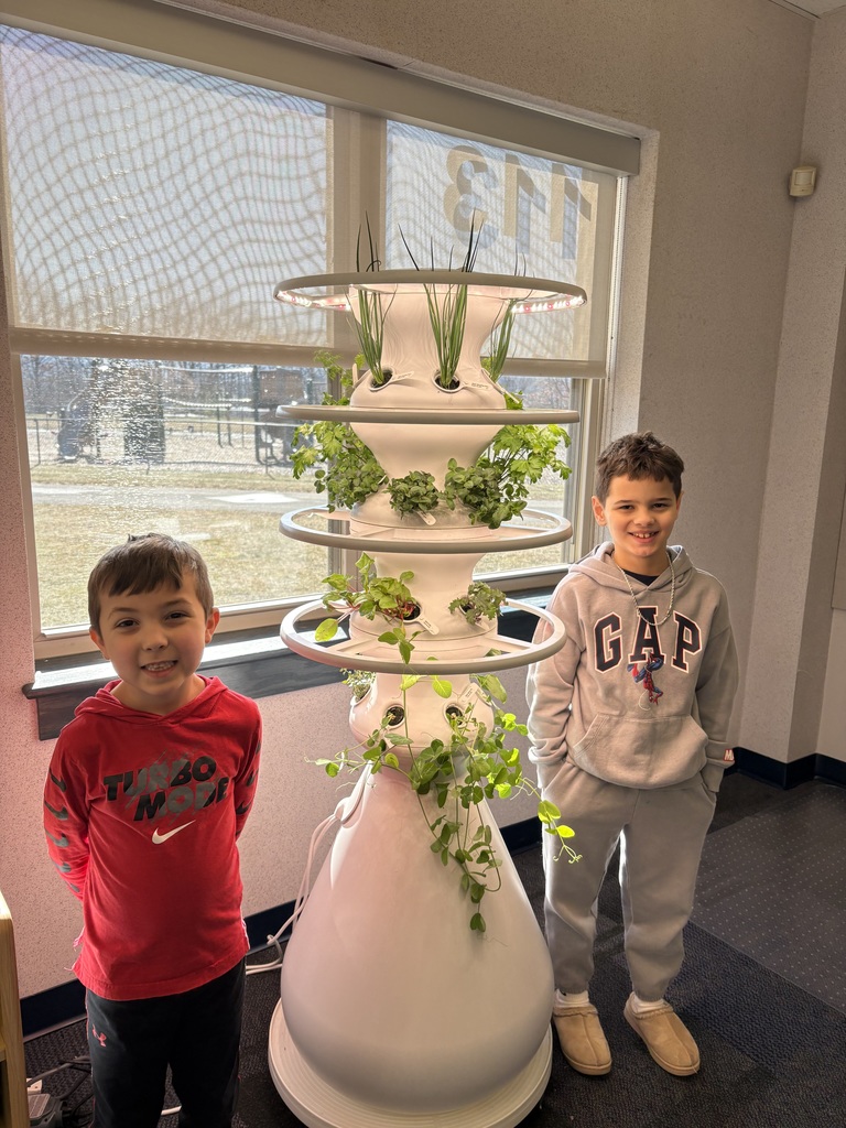 Students posing near hydroponic farm stand with lettuce growth and journals. 