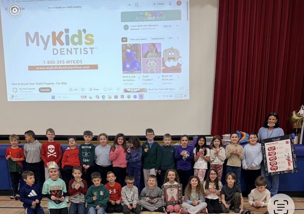 Mrs. baumes posing with a group of students with dental posters in the gym
