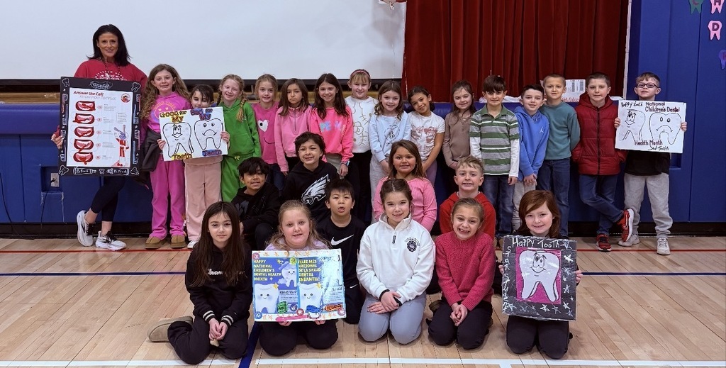 Mrs. baumes posing with a group of students with dental posters in the gym
