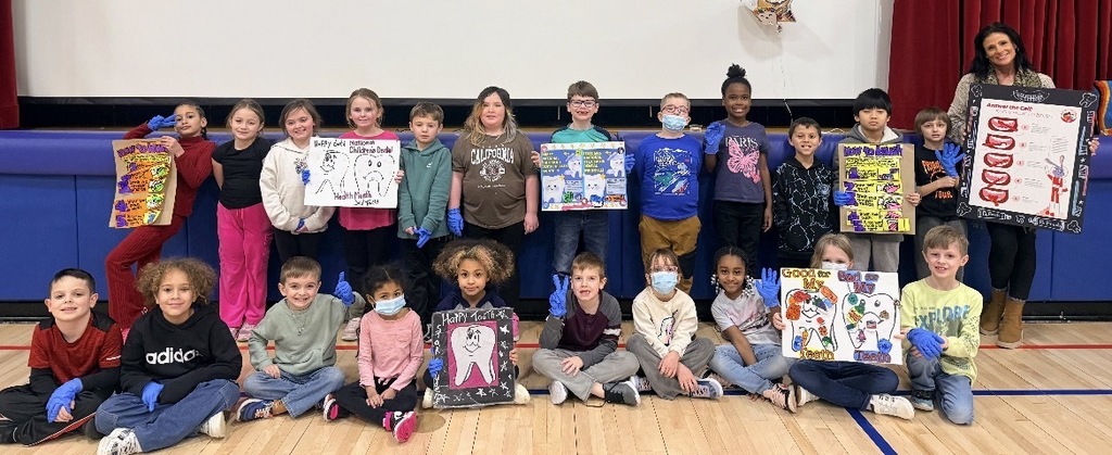 Mrs. baumes posing with a group of students with dental posters in the gym