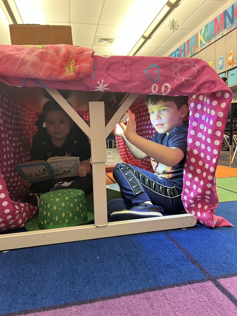 A blanket tent in a classroom with students reading books