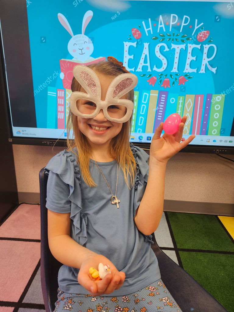 A student holding a plastic easter egg wearing bunny glasses. 