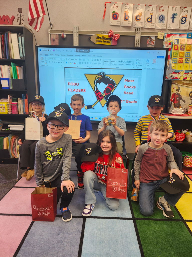 A group of students smilingv at the camera in front of a slide that says Robo Readers Most books read with a penguins hockey logo
