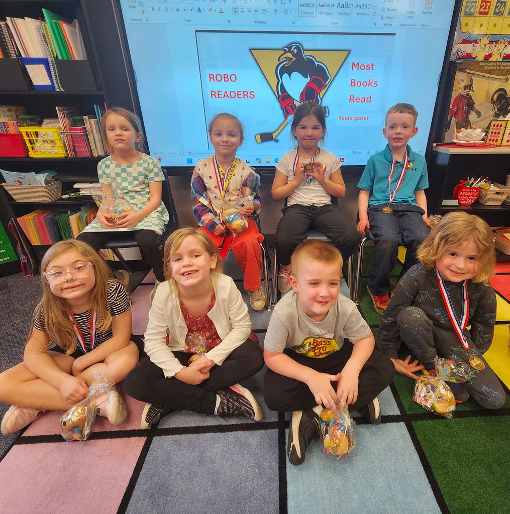 A group of students smilingv at the camera in front of a slide that says Robo Readers Most books read with a penguins hockey logo