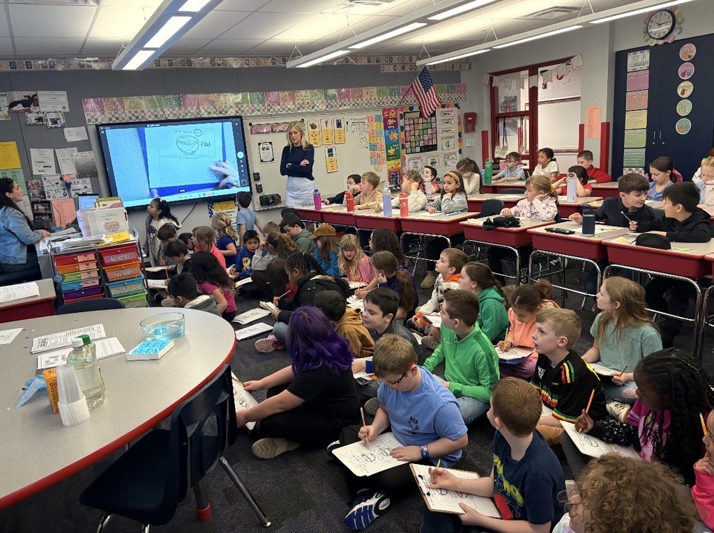 Students seated with clipboards observing blue marshmallow peeps in different liquids  