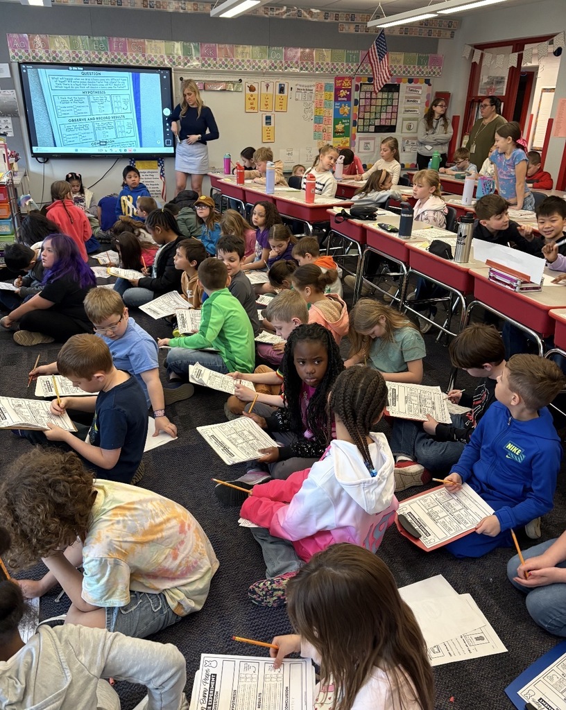 Students seated with clipboards observing blue marshmallow peeps in different liquids  
