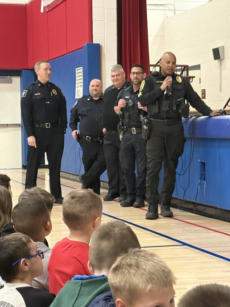 A group of 5 police officers in front of a class. 