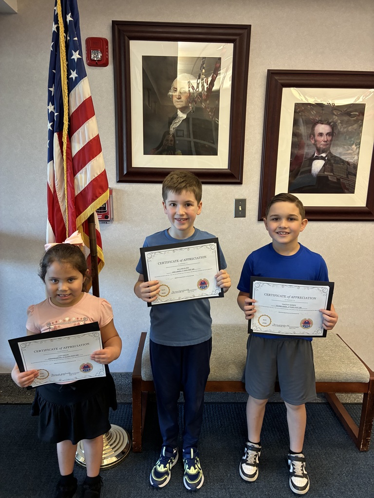 Three students holding amvets winner certificates in front of two president portraits and an american flag. 