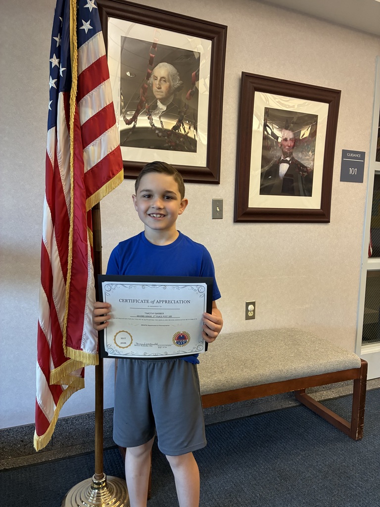 A student holding an amvets winner certificate in front of two president portraits and an american flag. 