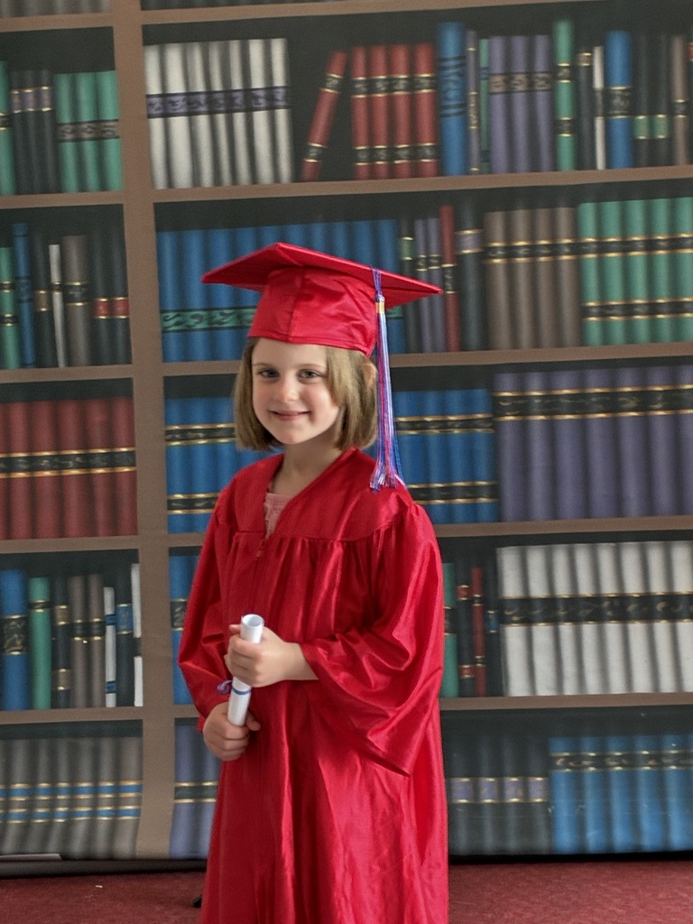 A girl wearing a red graduation gown and cap in front of a book backdrop