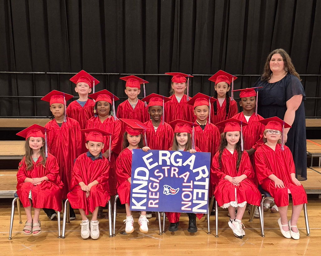 Kindergarten students in red caps and gown holding a kindergarten registration sign