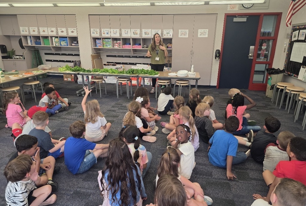 Students and teachers in the stem lab with hydroponic farm stands with lettuce and  flowers 