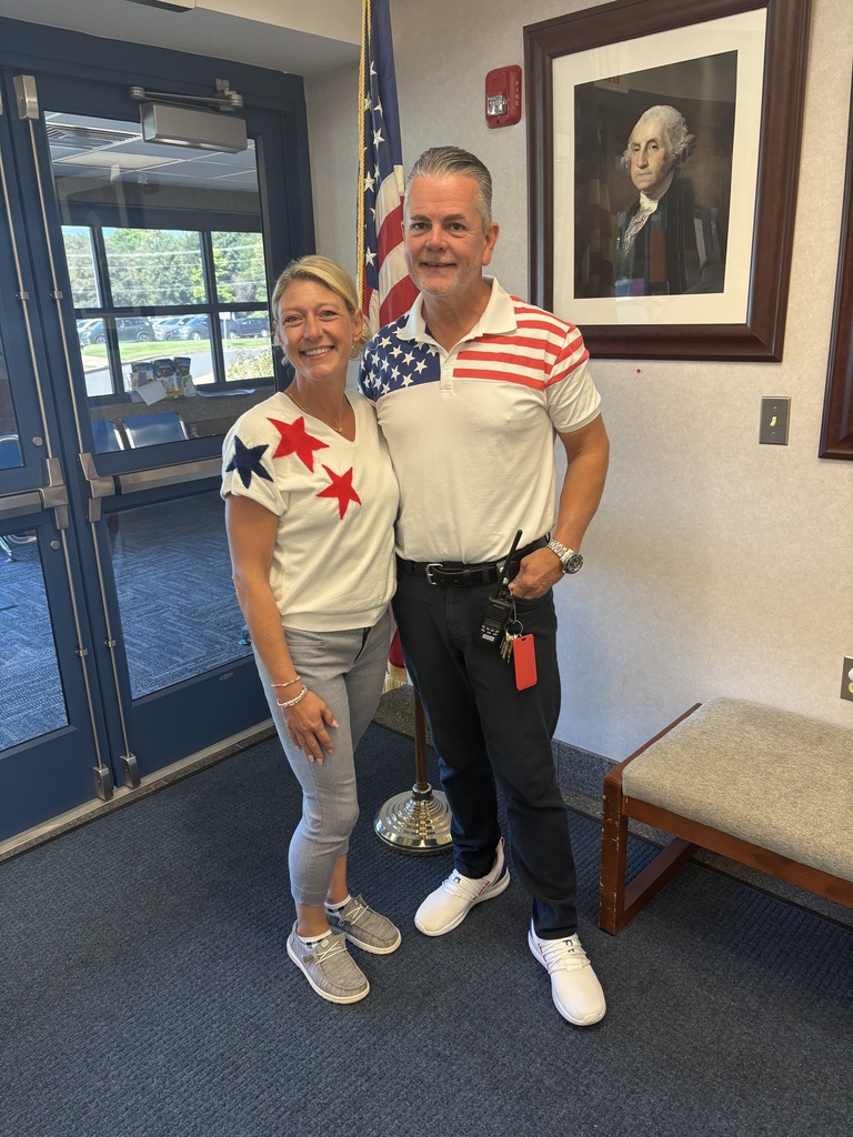 A woman and man posing infront of a flag in patriotic shirts.