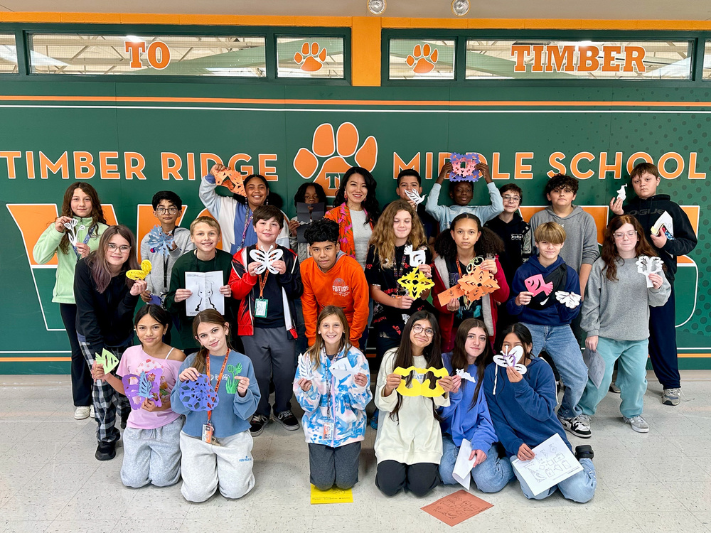 group of students holding paper cut artwork stand pose with artist