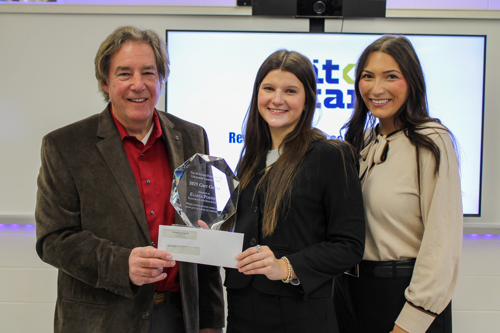 three people stand together. Man on left hands check to woman in middle
