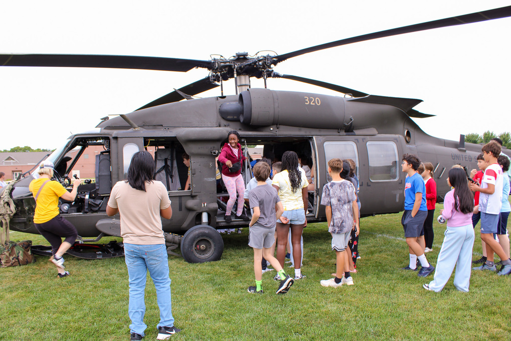 middle school students gather around a military helicopter
