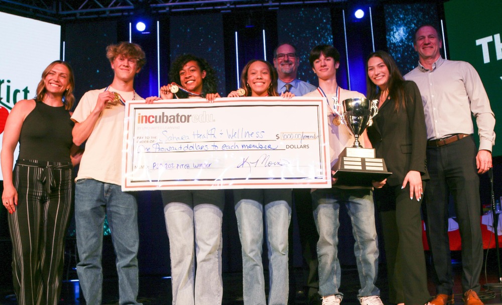 group of students stand on stage with adults holding oversize check