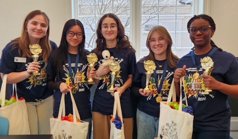 five girls wearing blue shirts old trophies and tote bags with colorful paper coming out of the top